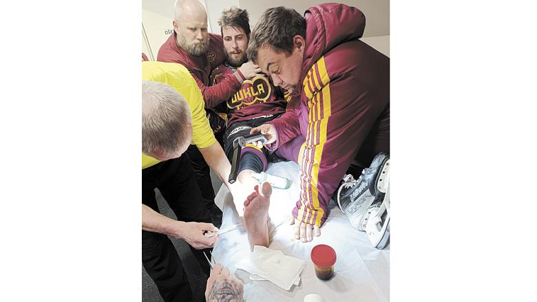 SLOVA trenéra Viktora Ujčíka o odhodlání jeho svěřenců překonat v play off zdravotní problémy potvrzuje snímek z šestého finále Maxa ligy. Doktor a zdravotnický štáb pracují na pochroumaném kotníku útočníka Radka Pořízka. Foto: Michal Boček 