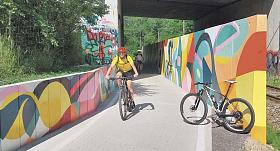 CYKLISTÉ projíždějí pod dálničním mostem po novém úseku cyklostezky od Stříteže k Pávovu. Mural artem vyzdobená protitlaková stěna tu chrání cyklisty před rázy od projíždějících vlaků.Foto: Jiří Varhaník 